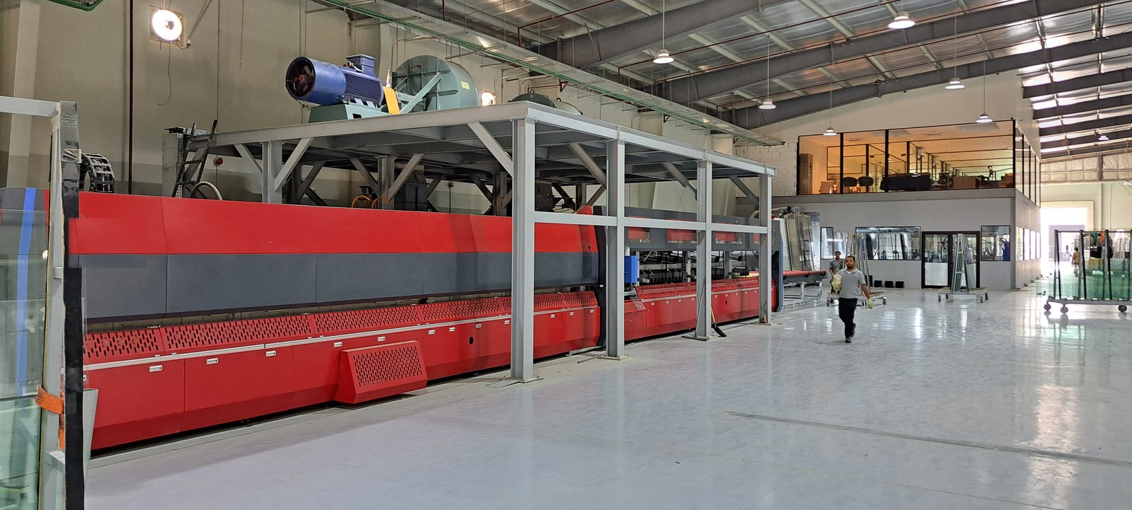 Red tempering-furnace line on the factory floor, glass racks and mezzanine offices beyond