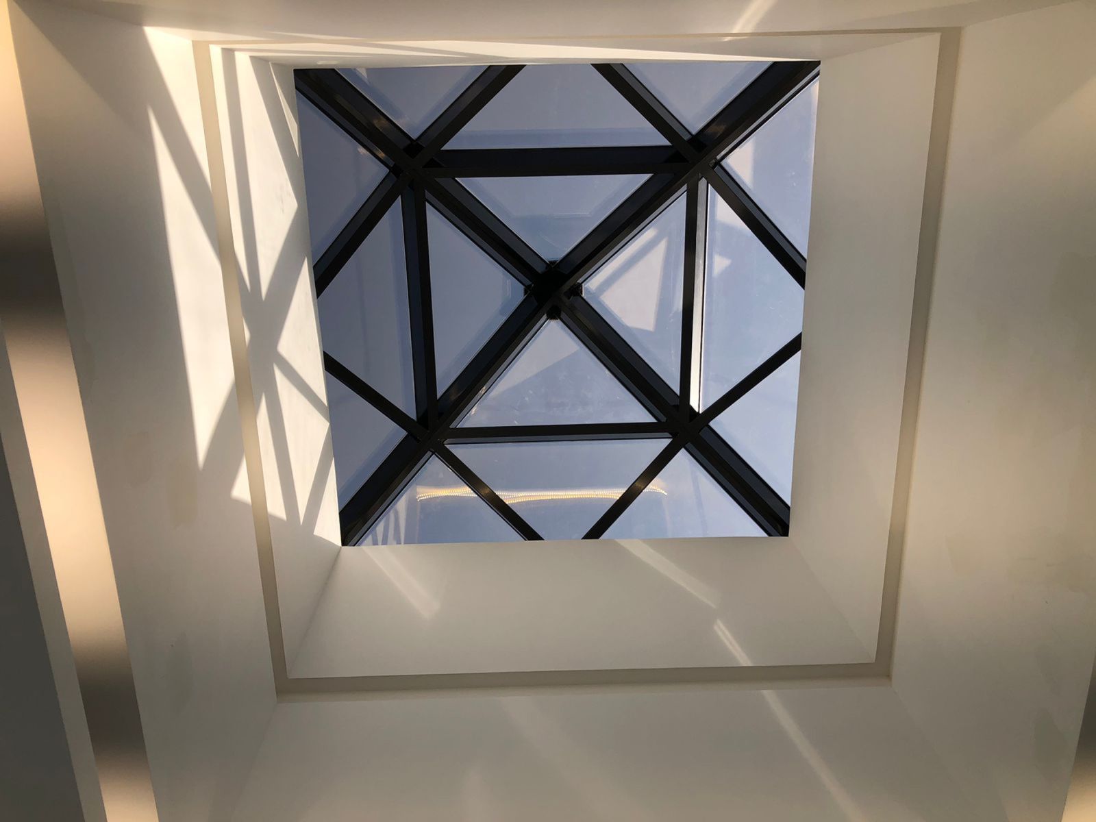 Square laminated-glass skylight in a triangulated black frame, seen from the atrium below
