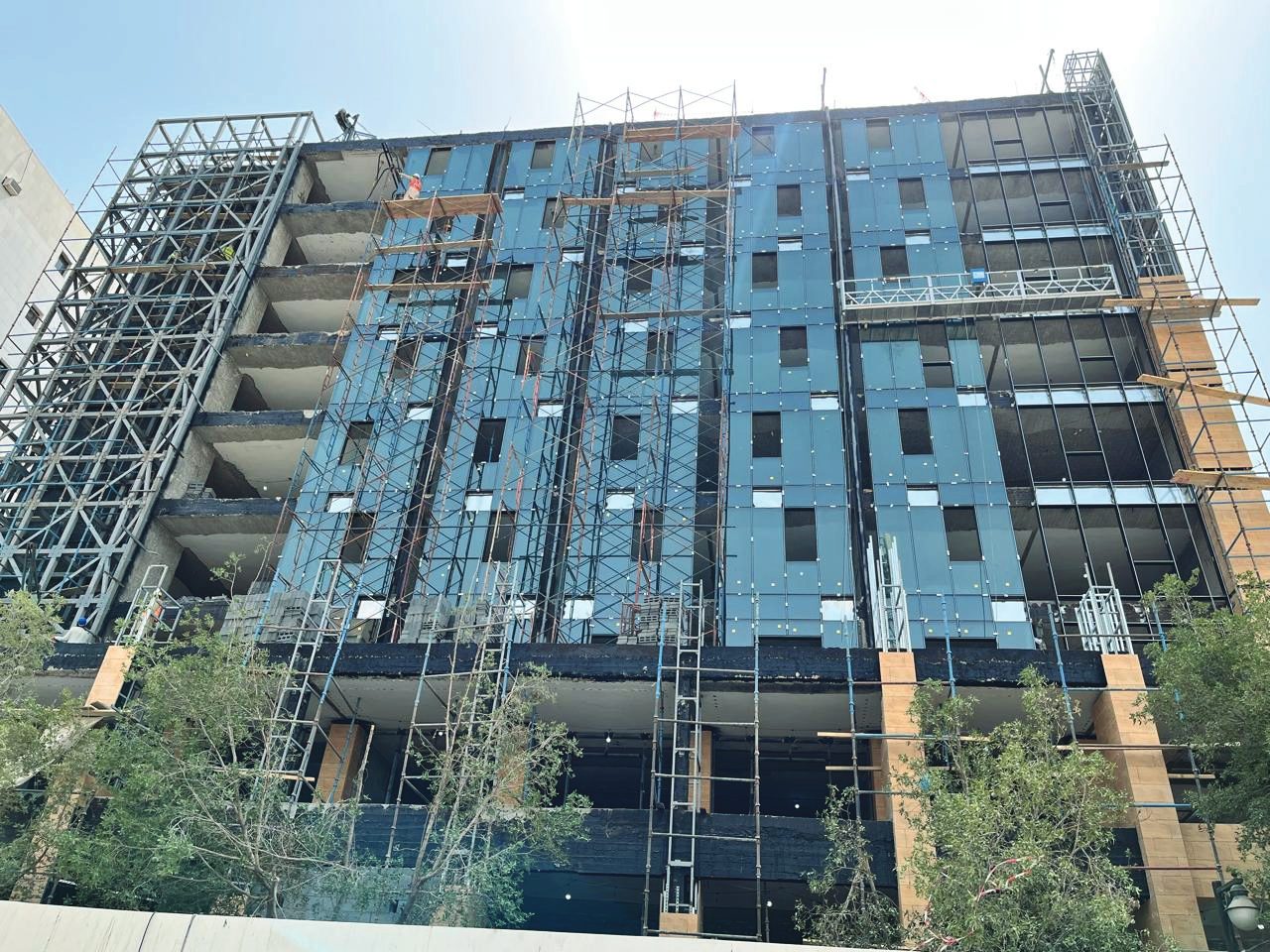 Marriott Hotel tower mid-construction, blue-grey curtain-wall panels going up behind scaffolding