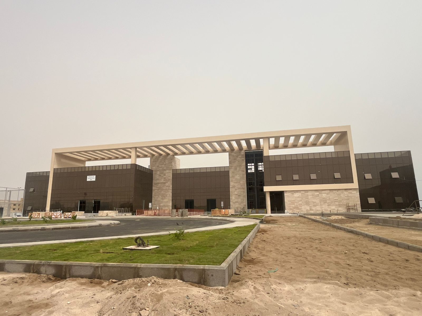 Low-rise campus with bronze glazing under a monumental stone pergola at the Rabigh Desalination Oasis