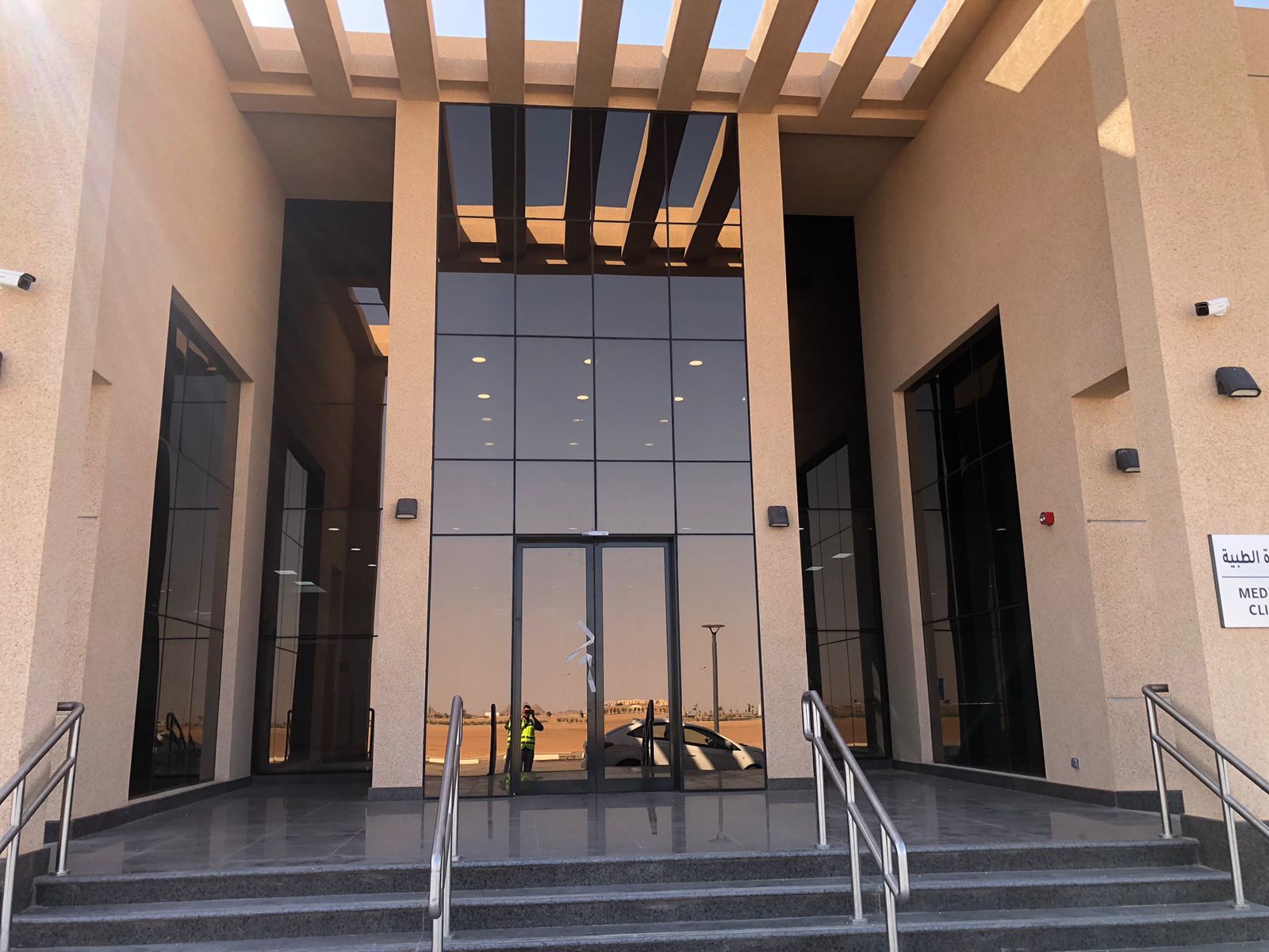 Tall dark structural glazing framing a stone entrance beneath a slatted pergola